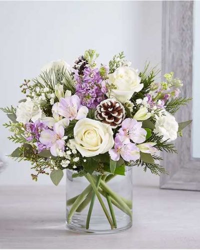 We’ve captured the peaceful beauty of winter in our lovely bouquet. A new seasonal version of our best seller, it’s loosely gathered with soothing lavender & white blooms, cascading greenery all around and pinecone accents for a rustic touch. A truly wonderful way to express your sentiments this time of year.
<ul>
 	<li>All-around arrangement with white roses and carnations; lavender Peruvian lilies (alstroemeria) and stock; accented with baby’s breath, seeded eucalyptus, pinecone picks and assorted Christmas greenery</li>
 	<li>Artistically designed a clear glass cylinder vase</li>
 	<li>Large arrangement measures approximately 15"H x 13"W</li>
 	<li>Medium arrangement measures approximately 13"H x 12"W</li>
 	<li>Small arrangement measures approximately 12"H x 9"W</li>
 	<li>Our florists select the freshest flowers available, so colors, varieties and container may vary due to local availability</li>
 	<li>To ensure lasting beauty, Peruvian lilies may arrive in bud form and will fully bloom over the next few days</li>
</ul>