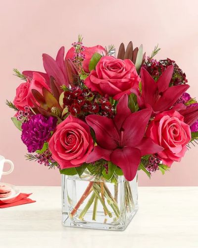 Radiant jewel tones set the tone for a romantic Valentine’s Day. Our eye-catching arrangement mixes classic roses and lilies with unique Leucadendron and dianthus. Gathered in a chic cube vase with lush touches of greenery, it’s a sweet and stylish expression of love.